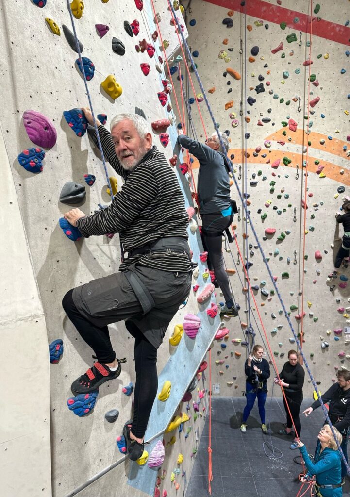 Two men on climbing wall being supported by safety ropes