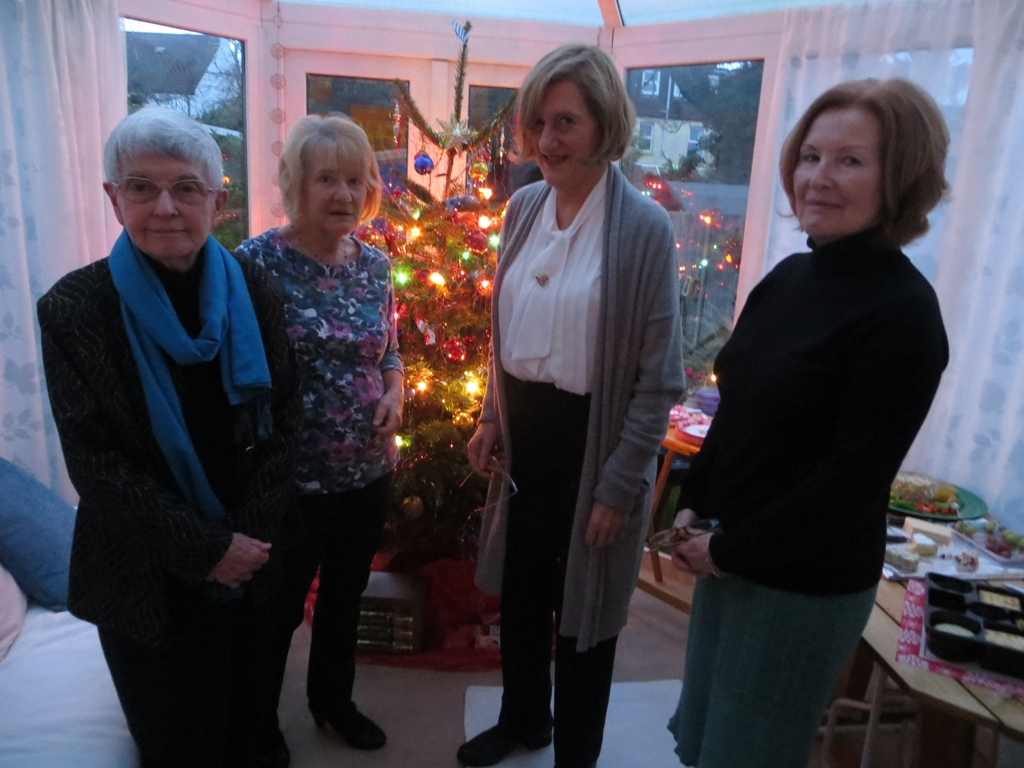 A room with four standing women posing for a photo in front of a Christmas tree