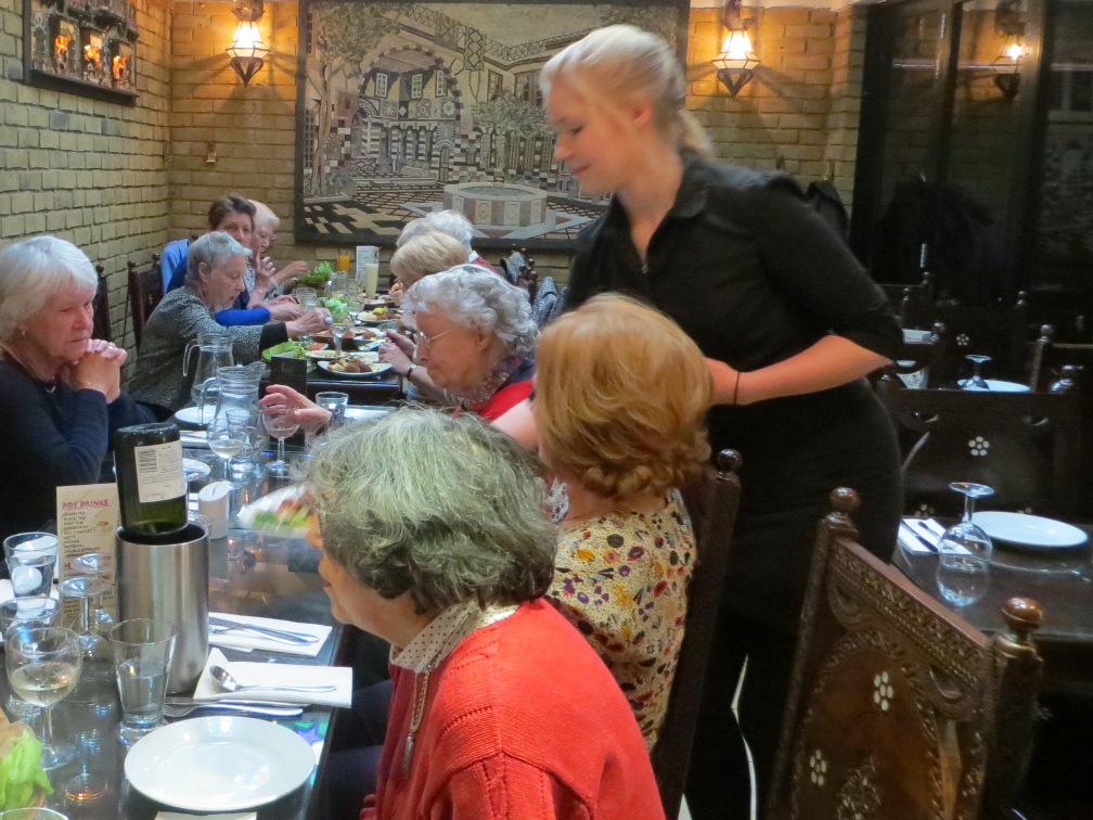 People seated at a table having a meal in a restaurant with a waitress serving one of them