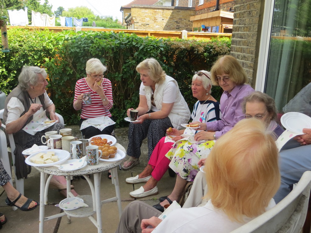 People seated around a table in a back garden, eating and drinking