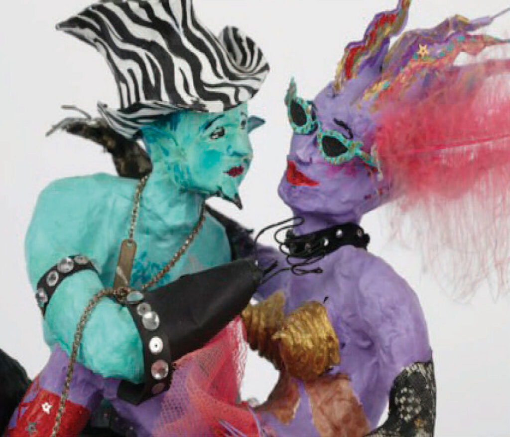 Two papier-mâché machista figures coloured turquoise and mauve, one wearing a black and white wiggly-striped hat, the other with a red feather in her 'hair' and wearing turquoise-coloured sunglasses
