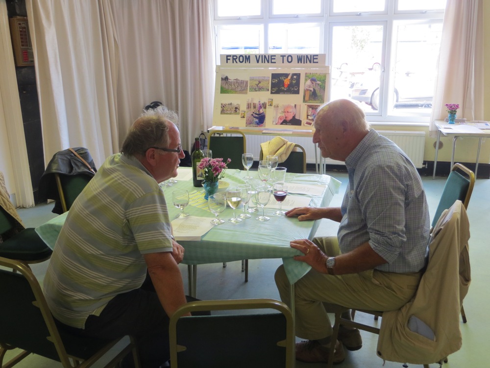 Two men in conversation, seated at a table, having a drink